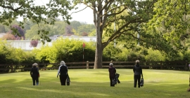 Four golfers walking on a green golf course.