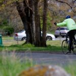 A resident participating in active transportation in Oak Bay, cycling in a lime green jacket signaling to turn left.