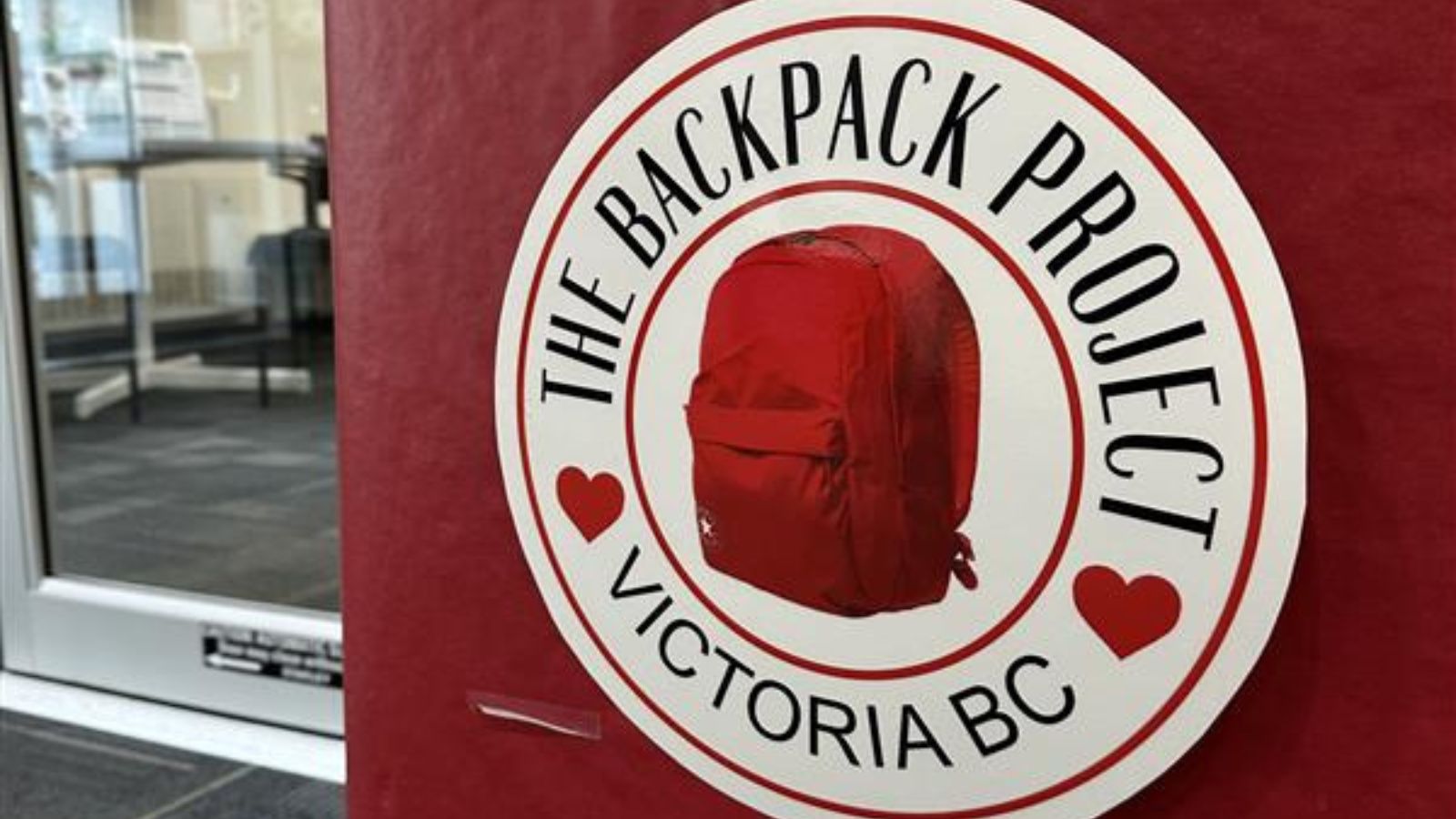 A red box in Oak Bay Municipal Hall's foyer with a red backpack on it, with hearts and a title reading "The Backpack Project, Victoria BC"