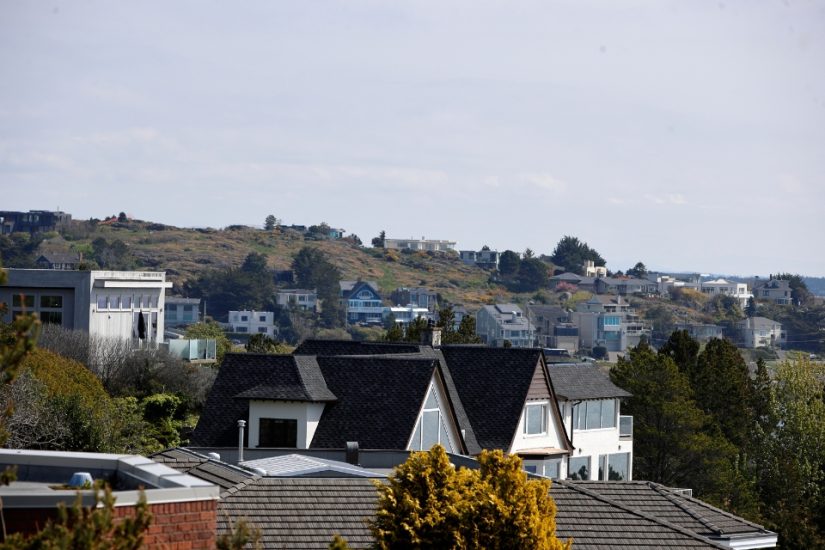 A landscape photo of houses across a gentle hill in Oak Bay, with trees lined between houses and light clouds on a sunny day.
