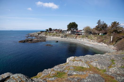 A small ocean bay is lined with a rocky coast and a few homes adjacent to the beach.